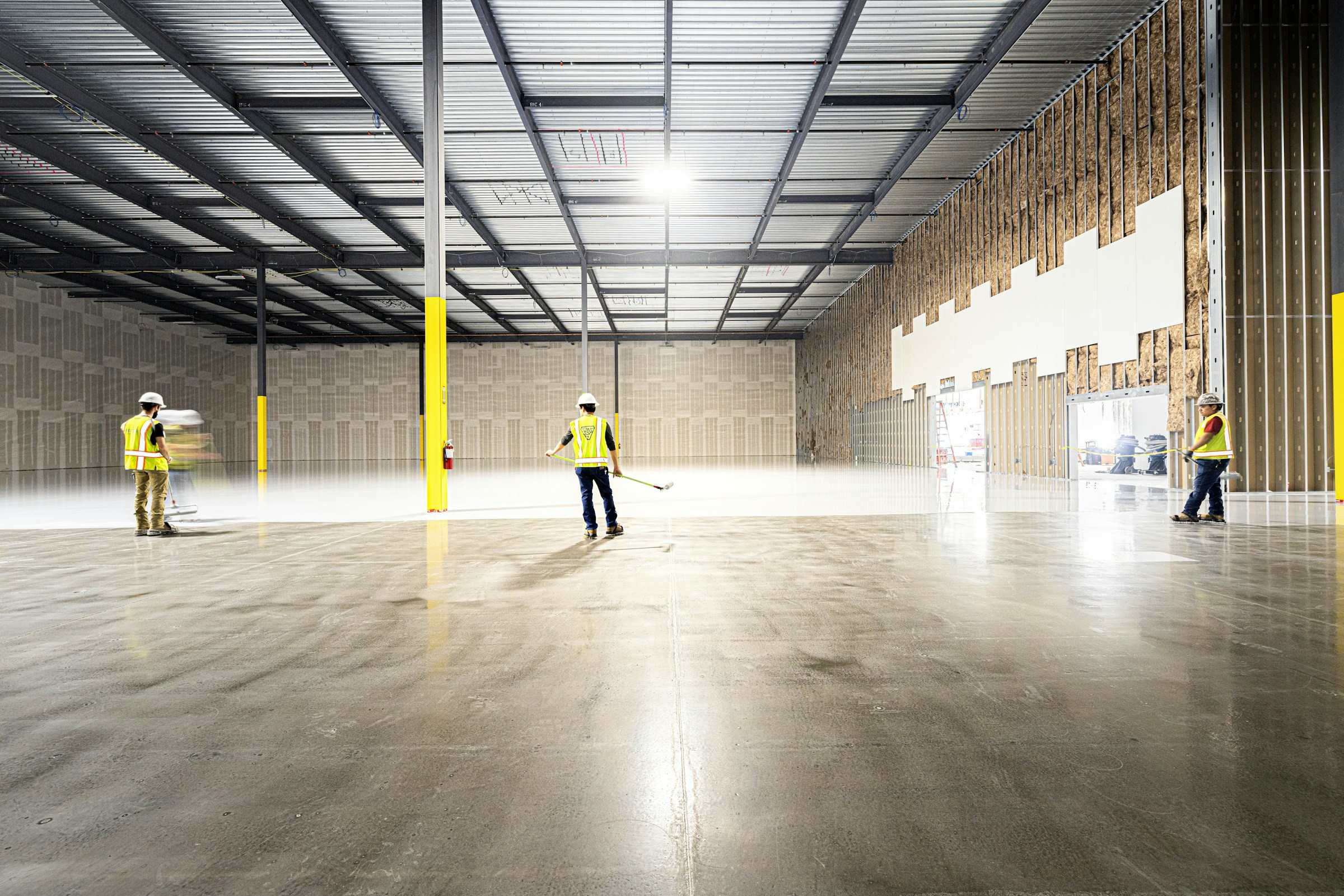 A crew in hard hats and safety vests finishing the floor of a large industrial building